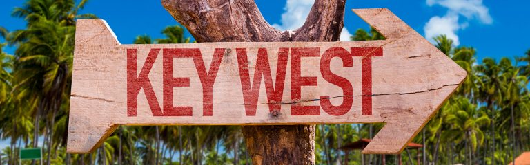 A wooden sign nailed to a tree pointing to Key West
